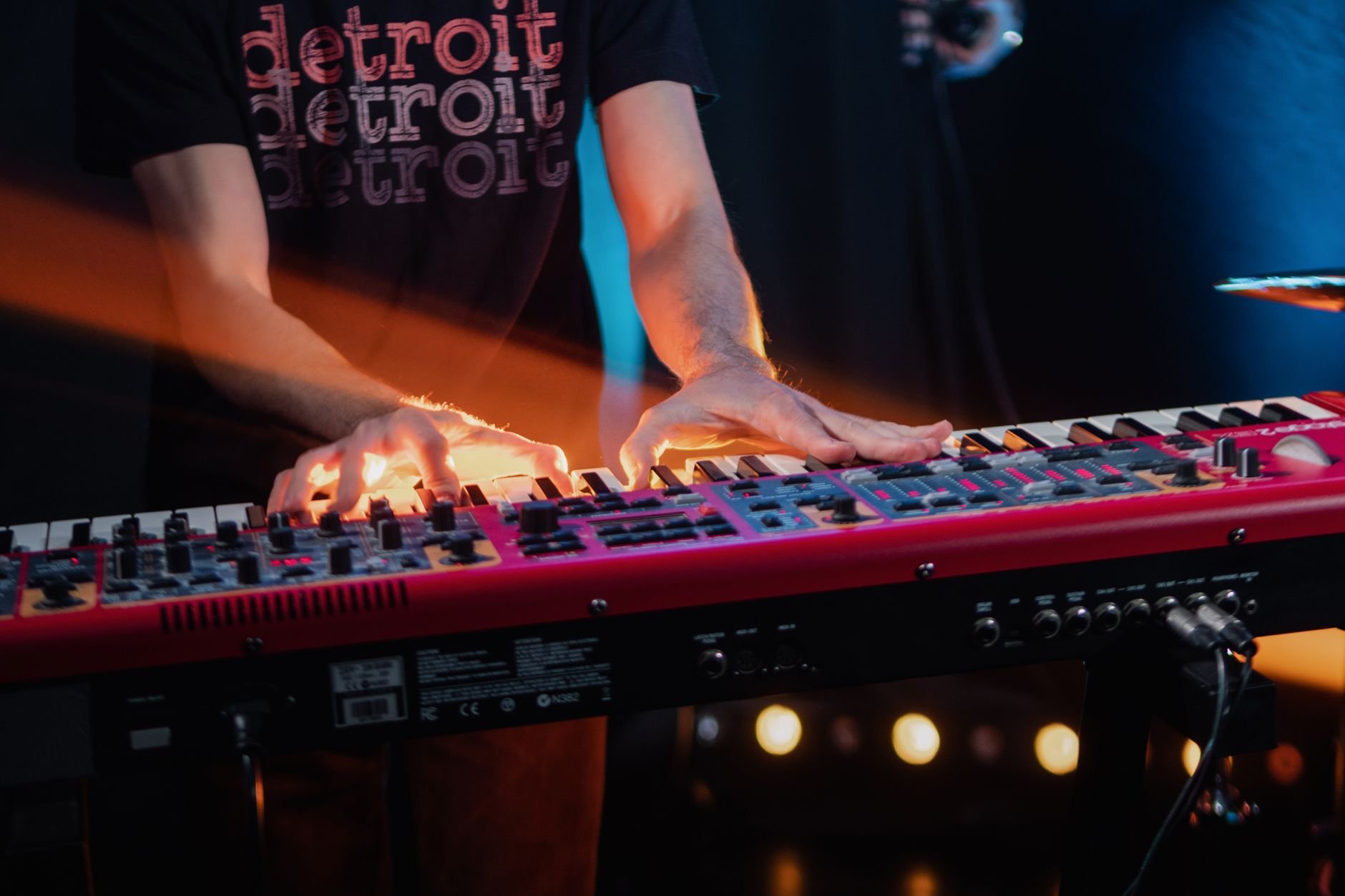 Close-up of a musician playing a keyboard on stage with vibrant light effects
